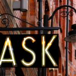 Storefront sign that says "ASK" in front of lamp and red building walls