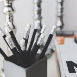 Close up shot of multiple black pencils in a cup with a notebook in the background